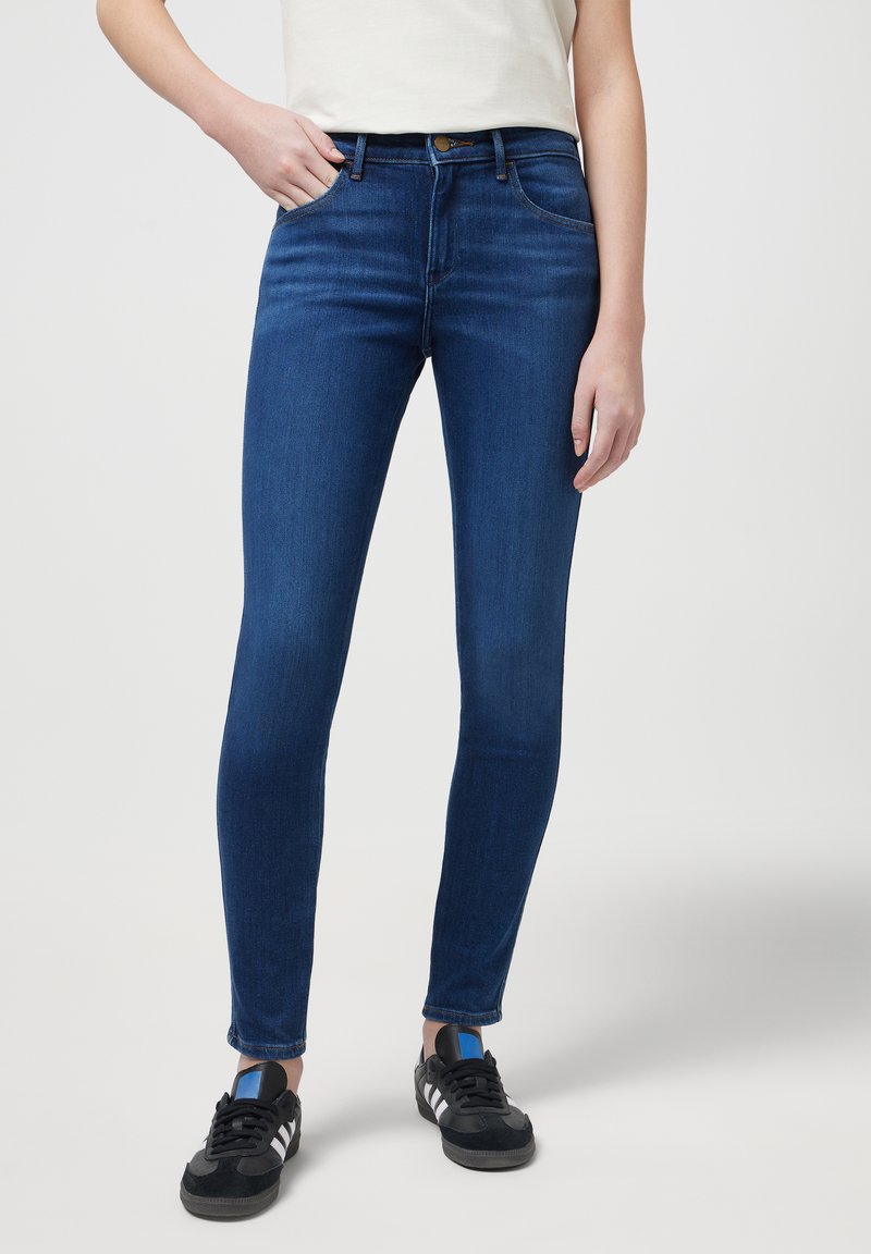 Jean skinny en denim bleu foncé avec une texture lisse, un design à cinq poches et une fermeture à bouton à la taille.