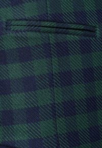 Fragment tkaniny w kratkę w ciemnozielonym i granatowym kolorze, z teksturowanym splotem o subtelnej poświacie i płaską kieszenią.