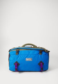 Sac de sport bleu et noir avec des accents verts, une poignée supérieure, une fermeture éclair, et des sangles violettes avec un patch logo à l'avant.
