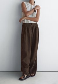 Haut sans manches gris clair associé à un pantalon en lin brun foncé à coupe ample. Des plis à la taille et des sandales plates rehaussent le look.