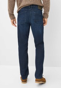 Jeans in denim blu scuro con taglio dritto. Presentano due tasche posteriori e una vita texturizzata. Indossati con scarpe in suede marroni.