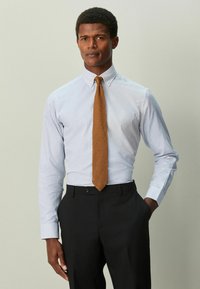 Vaaleansininen, ruudullinen pitkähihainen paita, jossa on kaulus, yhdistetty kuvioituun oranssiin solmioon ja mustiin housuihin, luoden liiketoimintaan sopivan muodollisen ilmeen.