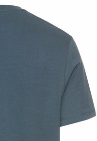 Bagtil af en ensfarvet mørkeblå t-shirt med korte ærmer, der viser skulder, ærmesøm og syninger på en lys baggrund.