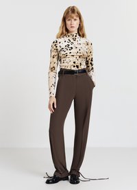 Maglietta a maniche lunghe con motivo leopardato beige e marrone, abbinata a pantaloni marroni a vita alta con coulisse ai polsini e cintura nera.