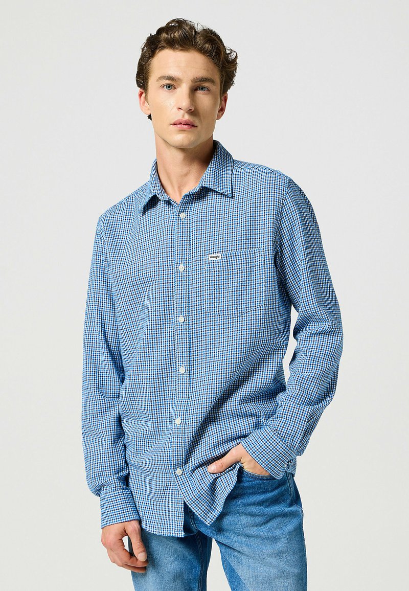 Camicia button-up a quadri blu e bianchi con taschino sul petto, realizzata in tessuto con una texture liscia. Presenta maniche lunghe e colletto.