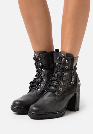 Bottines en cuir noir avec un talon empilé, un laçage à l'avant, une fermeture éclair sur le côté et des clous le long de la semelle. Tige texturée.