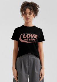 Zwarte katoenen t-shirt met een roze graphic waarop "LOVE est. 1994." staat. Gecombineerd met grijze hoge taille broeken.