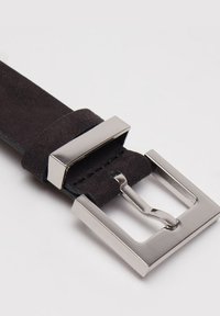 Černý semišový pásek se stříbrnou obdélníkovou kovovou sponou. Spona má jednoduchý, lesklý design a je přišita nití.