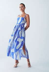 Sininen kuvioitu maxi-mekko, jossa on ohuet hihnat, istuvuus bodice ja virtaava hame, jossa on sivureikä. Sileä kangas rakenne korostaa muotoilua.