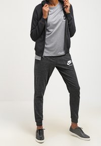 Černá zipová mikina přes šedé tričko, doplněná tmavě šedými tepláky s bílým logem Nike a černými teniskami s bílou podrážkou.