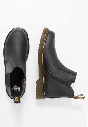 Bottines en cuir noir avec une finition lisse, fermeture éclair sur le côté, coutures jaunes et semelle en caoutchouc présentant un motif de semelle texturé.