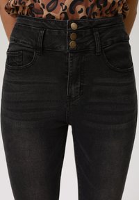 Jeans negros de cintura alta en tejido de denim con una textura suave, que presentan tres botones dorados en la cintura y bolsillos delanteros.