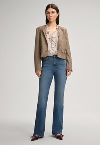 Bruine geruite cropped blazer over een lichtbeige bloes met ruches, gecombineerd met donkerblauwe flared jeans en bordeauxrode hoge hakken.