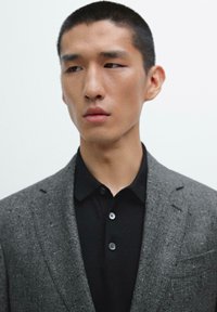 Gray woven blazer over a black collared shirt. The blazer has a textured appearance with structured shoulders and two buttons. Plain background.