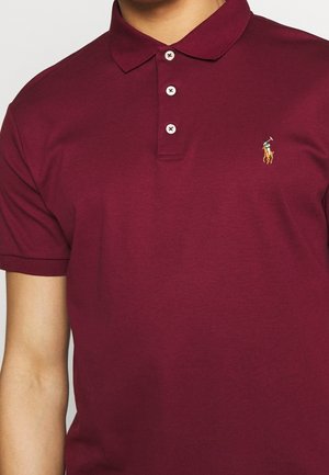 Bordowa koszulka polo z trzema białymi guzikami i małym haftowanym logo przedstawiającym gracza polo na koniu na lewej piersi.