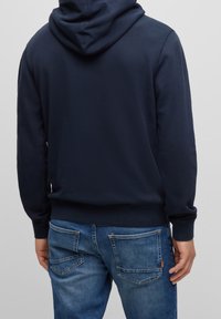 Navy blue hoodie with a drawstring hood, ribbed cuffs and hem, made of soft material. Paired with faded blue jeans featuring back pockets.