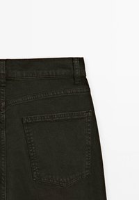 Schwarze Jeans aus Denim mit hoher Taille, sichtbaren Nähten und einer einzelnen Rückentasche mit spitzem Klappe. Glatte Textur, minimalistisches Design.