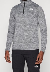 Grau melierter Pullover mit hohem Kragen und Viertel-Reißverschluss. Der Stoff ist strukturiert mit dezenten Sprenkeln und zeigt ein kleines weißes Logo auf der Brust.