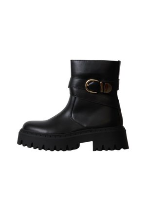 Bottine en cuir noire avec semelle épaisse à crampons et détail d'une bride avec boucle dorée sur le côté.