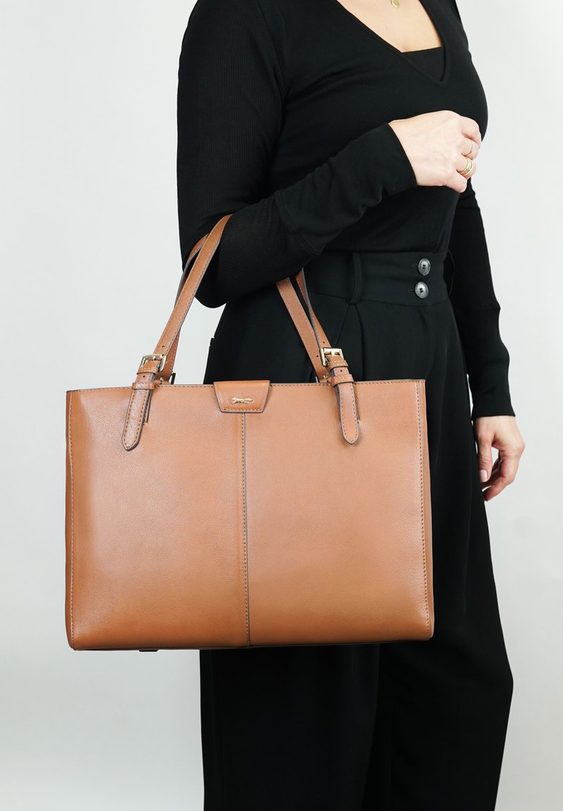 Bruine leren schoudertas met dubbele handvatten, een gladde textuur en een gestructureerde rechthoekige vorm. Voorzien van een eenvoudige voorklepsluiting en subtiele branding.