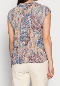 Mönstrad blus i flera färger med paisley-mönster och korta ärmar, som har en rynkad halsringning och ett flödande tyg. Bakdesignen betonar de livfulla färgerna.