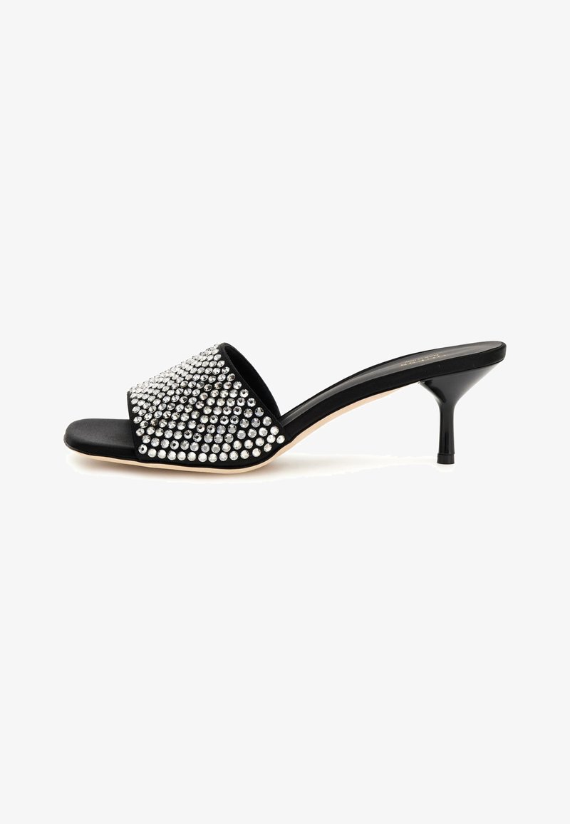 Musthave must väike rihmaga sandaal, millel on laiem rihm, millel on hõbedased nupud. Omab stiletto kontsa ja siledat, tugevat musta tallat.