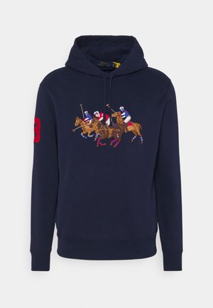 Granatowa bluza z kapturem z dużym haftowanym wzorem przedstawiającym trzech zawodników polo na koniach oraz czerwonym numerem 3 na prawym rękawie.