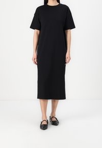 Robe maxi noire à manches courtes en tissu lisse, à coupe décontractée et col rond, assortie à des chaussures noires avec des lanières.