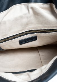 Zwarte leren tasinterieur met een crèmekleurige voering. Beschikt over een gouden rits en een zwart label met ‘DIEGO GOLDRENNER’ geperst.