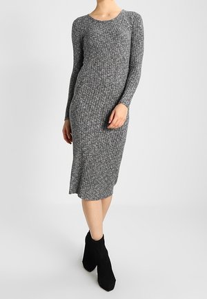 Abito a maglia grigio a coste con maniche lunghe, lunghezza fino al ginocchio, scollo rotondo e design aderente. Indossato con stivaletti neri.