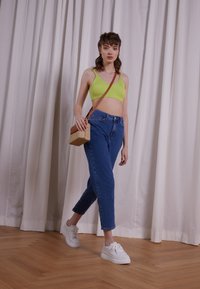 Un crop top côtelé vert lime, un jean bleu taille haute, des baskets blanches et un petit sac texturé avec une bandoulière marron, disposés sur un sol en bois.
