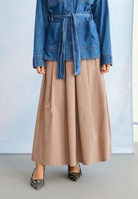 Jachetă din denim cu curea peste pantaloni bej largi și tocuri ascuțite alb-negru cu imprimeu de zebră pe o persoană în picioare.