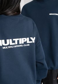 Felpa blu navy con un grande logo frontale in testo bianco, realizzata in tessuto morbido e con una vestibilità rilassata. Collo e polsini a coste.