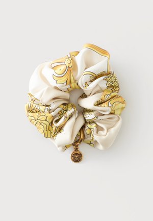 Coletero de seda con patrón barroco floral amarillo y un pequeño colgante dorado con cabeza de Medusa sobre un fondo blanco.