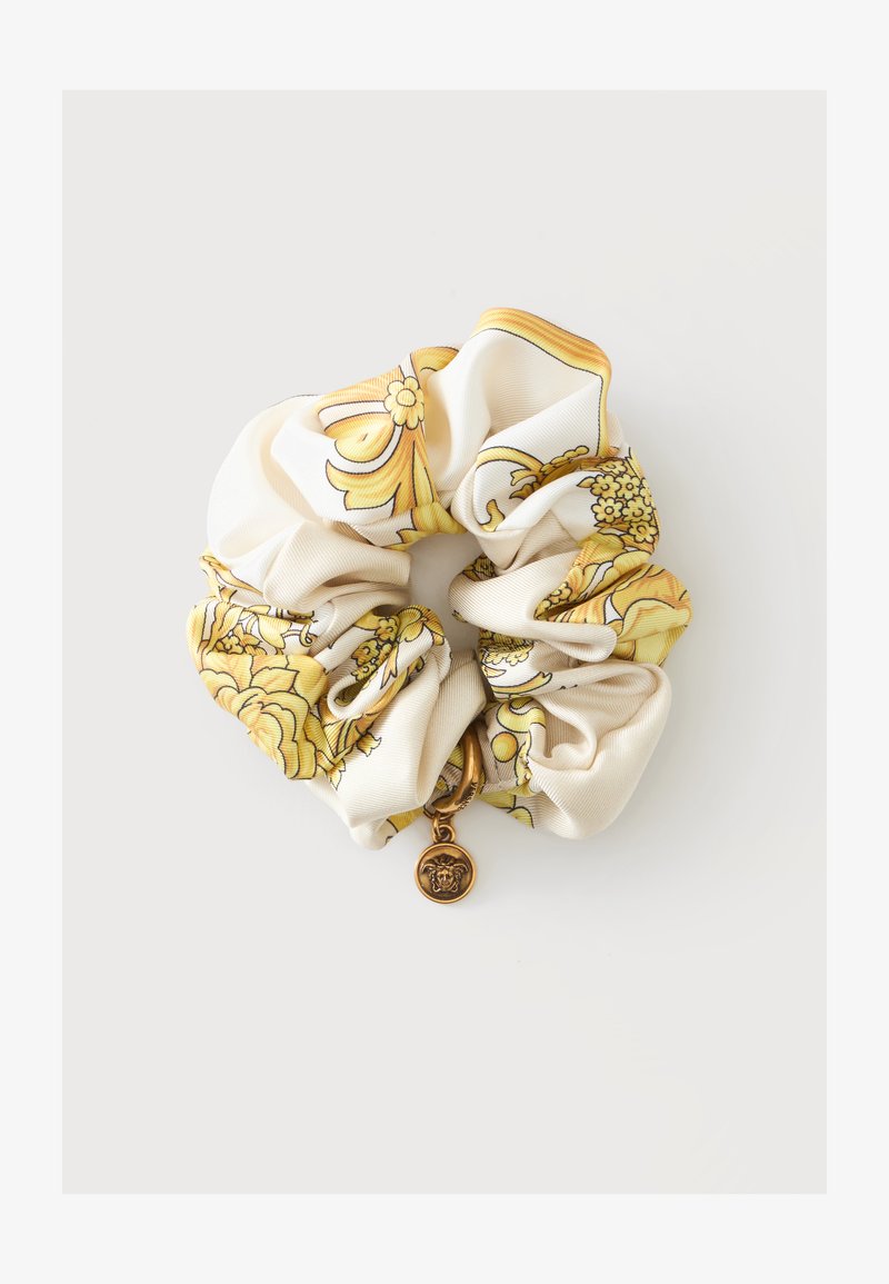 Chouchou en soie avec motif baroque floral jaune et petit pendentif tête de Méduse en or sur fond blanc.