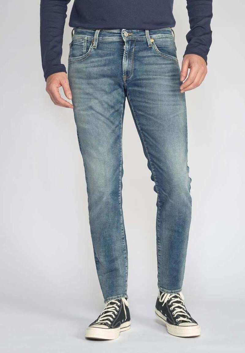 Jeans en denim bleu délavé avec une coupe slim, un design à cinq poches et des coutures contrastées, associés à des baskets montantes noires.