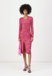 Rosa Leopardenmuster Kleid mit langen Ärmeln und taillierter Silhouette sowie einem knielangen Schlitz. Ergänzungen sind eine rosa Handtasche und schwarze Sandalen mit Riemchen.