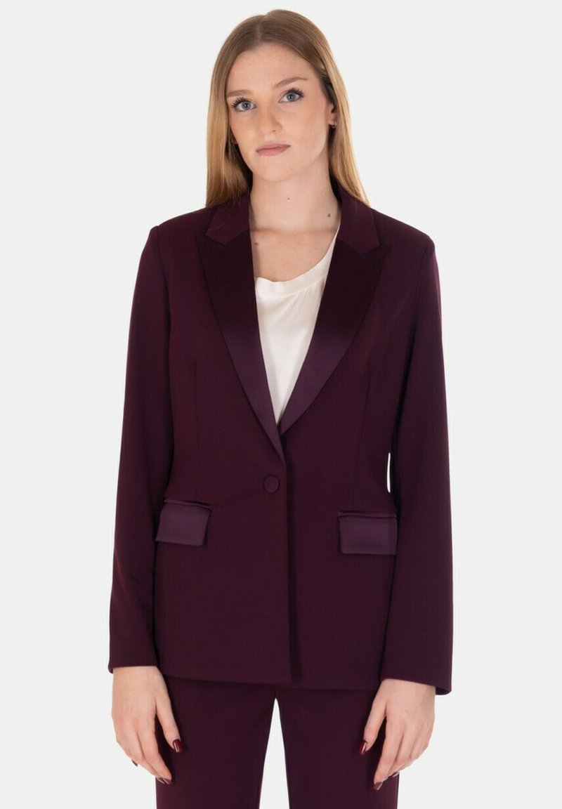 Blazer bordeaux con risvolti in satin, chiusura a un bottone, due tasche frontali, vestibilità strutturata e texture liscia, abbinato a un top crema.