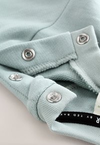 Tissu bleu clair à texture côtelée, avec des boutons-pression argentés et une étiquette avec un texte noir près du bord.