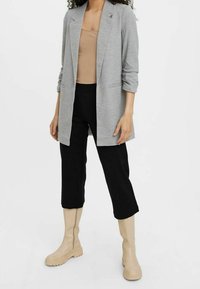 Szary żakiet z podwiniętymi rękawami, beżowy top na ramiączkach, czarne spodnie 3/4 i beżowe kozaki za kolano. Cechuje się luźnym krojem i minimalistycznym designem.