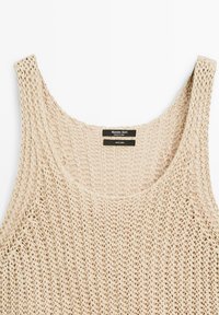 Canotta in lino beige con design a maglia larga e scollo ampio. Presenta un'etichetta con informazioni sul marchio e sulle cure sul retro.