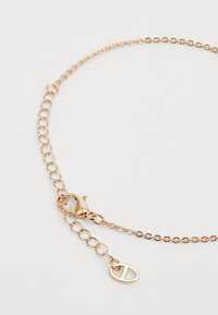 Gold-toned chain bracelet featuring oval links, a lobster clasp, and a charm with a stylized letter "D." Smooth, polished finish.
