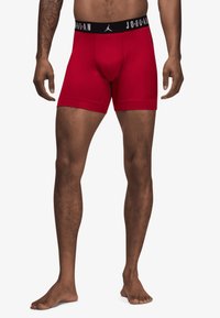 Røde boxer shorts lavet af strækbart stof, med en sort elastikbane med "JORDAN" logo og tætsiddende design. Blød tekstur, mellemlang længde.