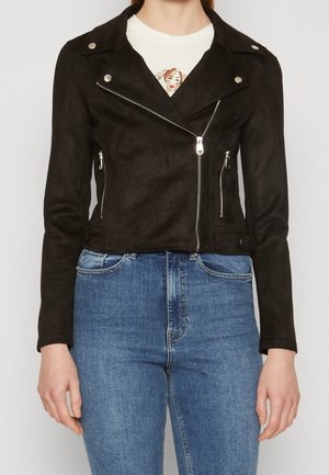 Czarna kurtka motocyklowa zamszowa z srebrnymi zamkami błyskawicznymi, kołnierzem z wycięciem, bocznymi kieszeniami oraz krótkim fasonem, zestawiona z niebieskimi dżinsami.