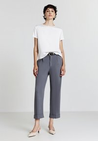 Top bianco a maniche corte abbinato a pantaloni grigi a vita alta, con una cintura visibile, e tacchi color crema con dettaglio a fiocco.