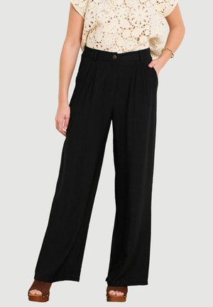 Woman wearing high-waist black wide-leg pants with pleats, paired with a cream crochet short sleeve top and brown platform sandals.