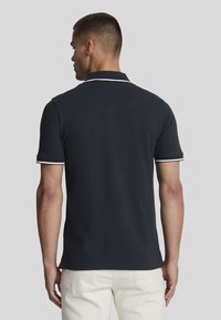 Svart poloskjorte med hvite detaljer, kort erm, og klassisk krage, med en jevn tekstur og en figursydd design.