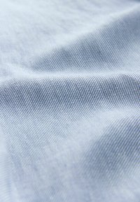 Tela azul claro con una textura suave y un patrón de nervaduras diagonales, mostrando sutiles variaciones de color en toda la superficie.