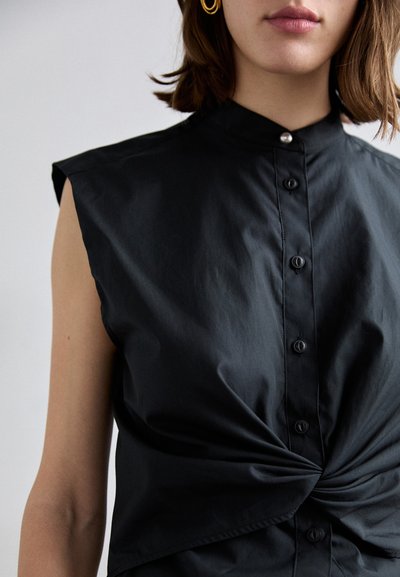 Tricou negru fără mâneci, cu guler înalt, închidere frontală cu nasturi și detaliu de nod răsucit la talie, fabricat dintr-un material neted.