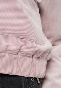 Ανοιχτό ροζ πουλόβερ από κορδούρα με υφασμένους κατακόρυφους λοξούς και λεπτομέρεια στη συγκεντρωμένη ραφή στο τελείωμα, συνδυασμένο με σκούρο τζιν, εμφανίζοντας μια απαλή, ζεστή εμφάνιση.